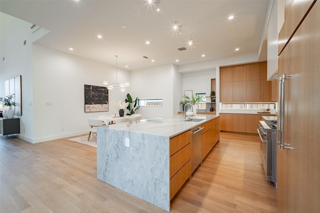 kitchen with pendant lighting, a large island with sink, light stone counters, stainless steel appliances, and light wood-type flooring