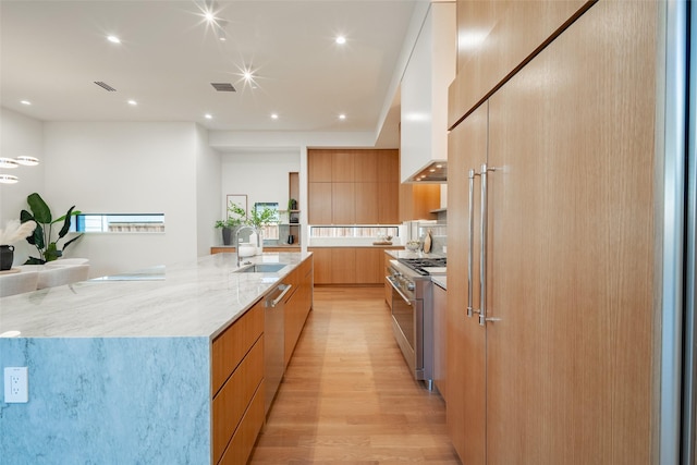 kitchen featuring premium appliances, light stone counters, a sink, wall chimney range hood, and modern cabinets