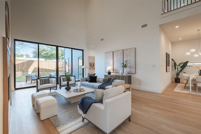 living area featuring baseboards, a high ceiling, visible vents, and light wood-style floors