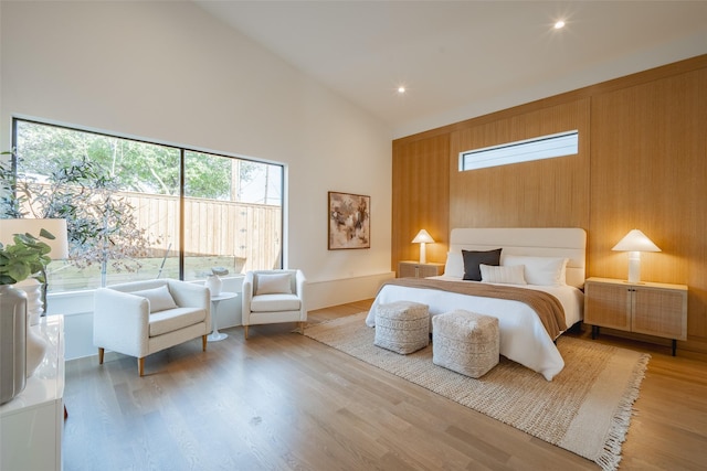 bedroom with wood walls, high vaulted ceiling, and light wood-type flooring