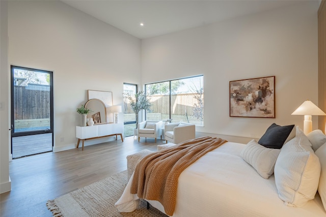 bedroom featuring access to exterior, a high ceiling, baseboards, and wood finished floors