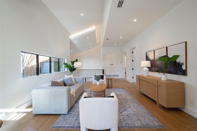 living area with recessed lighting, visible vents, a towering ceiling, and light wood finished floors