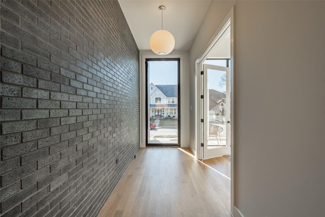 doorway to outside with brick wall, baseboards, and light wood-style flooring