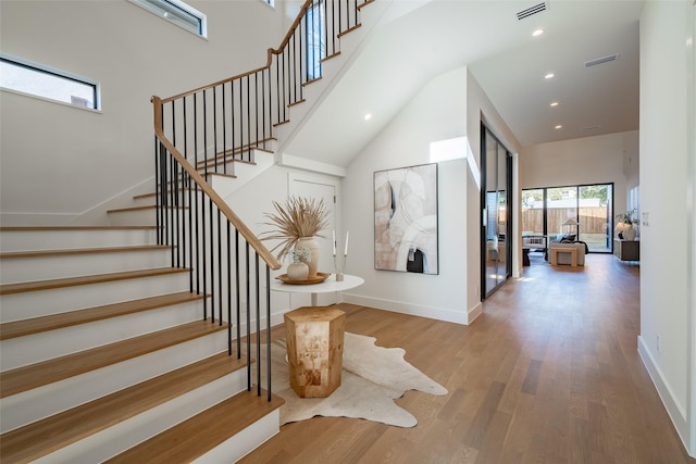 stairway with a towering ceiling, visible vents, baseboards, and wood finished floors