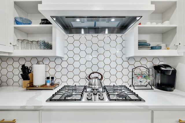 kitchen with wall chimney exhaust hood, stainless steel gas cooktop, white cabinetry, light stone countertops, and decorative backsplash