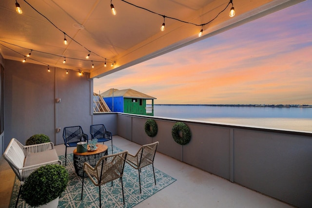 balcony at dusk with a patio area, outdoor lounge area, and a water view