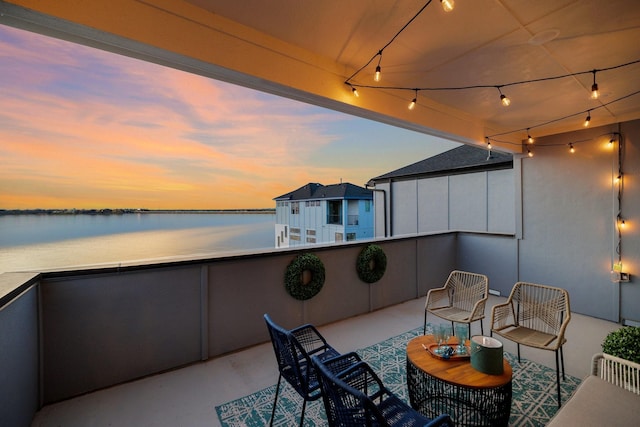 balcony at dusk featuring a water view