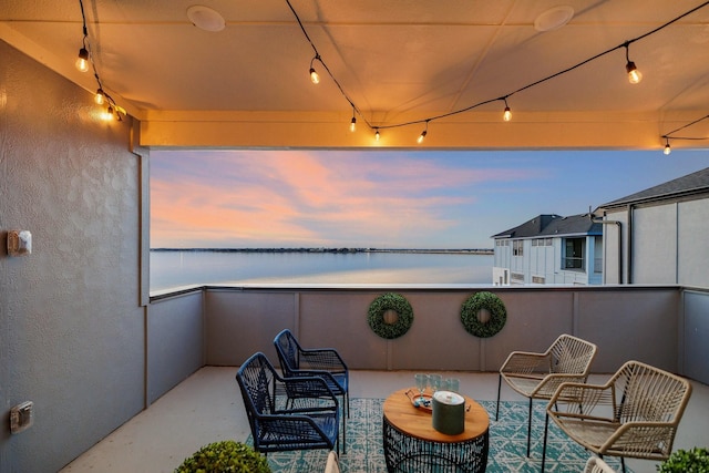 patio terrace at dusk featuring a water view and a balcony