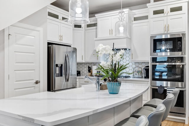 kitchen with a kitchen bar, pendant lighting, stainless steel appliances, decorative backsplash, and white cabinets