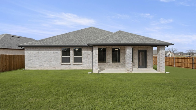 back of property with a shingled roof, a patio, a fenced backyard, a yard, and brick siding