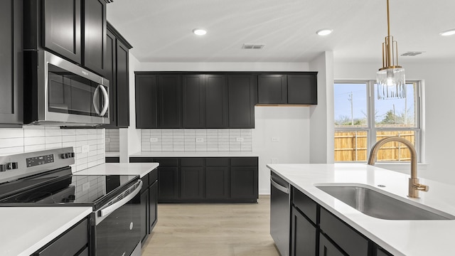 kitchen featuring stainless steel appliances, light countertops, a sink, and dark cabinets