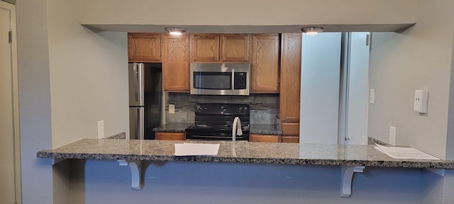 kitchen featuring a kitchen breakfast bar, dark stone counters, decorative backsplash, kitchen peninsula, and stainless steel appliances