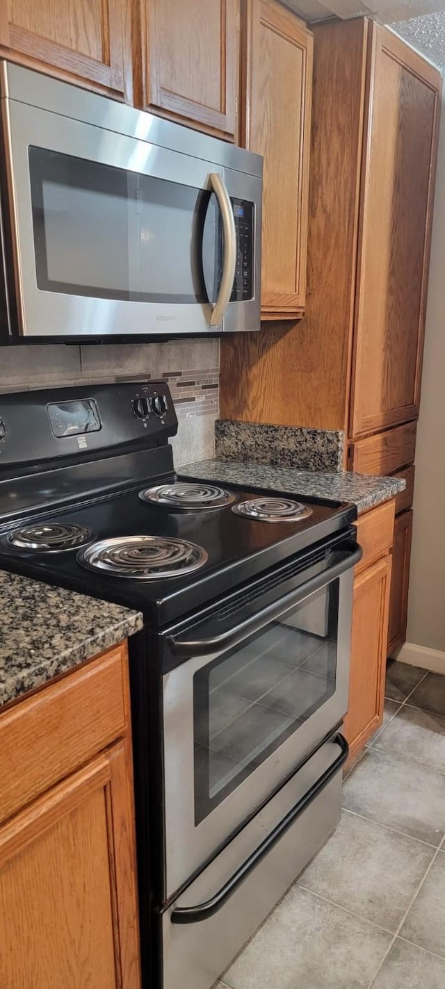 interior space with light tile patterned floors, stainless steel appliances, and dark stone counters