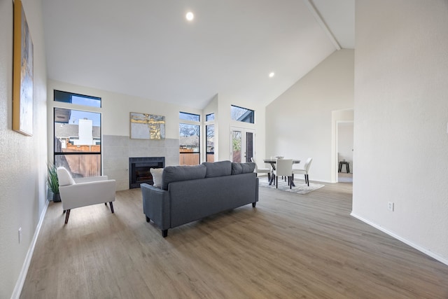 living room featuring high vaulted ceiling, plenty of natural light, hardwood / wood-style floors, and a tile fireplace