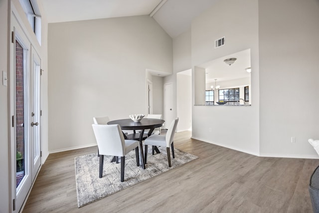 dining area with hardwood / wood-style flooring, a notable chandelier, and high vaulted ceiling