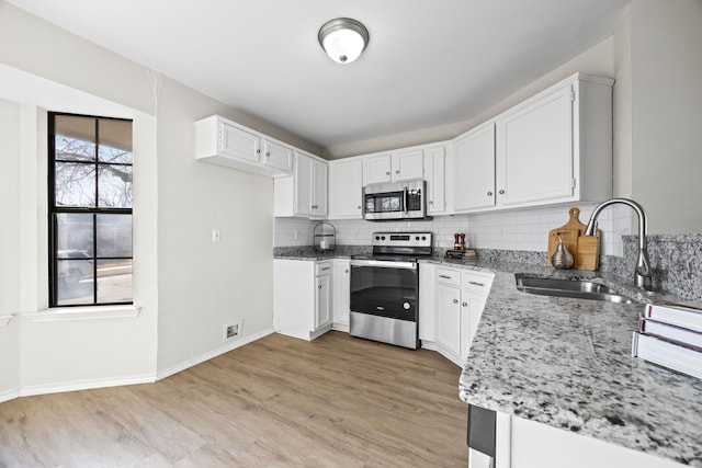 kitchen featuring sink, white cabinetry, light wood-type flooring, appliances with stainless steel finishes, and light stone countertops