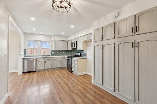 kitchen with appliances with stainless steel finishes, sink, a chandelier, decorative backsplash, and light hardwood / wood-style flooring