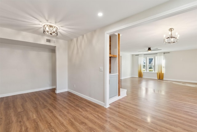 spare room featuring wood-type flooring and ceiling fan with notable chandelier