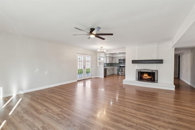 unfurnished living room with ceiling fan with notable chandelier, hardwood / wood-style floors, a fireplace, and french doors