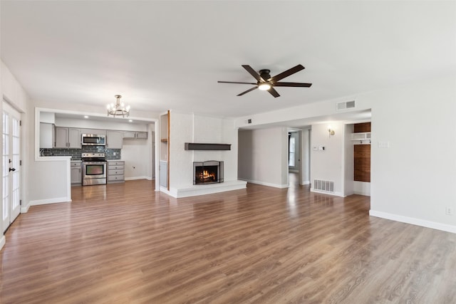 unfurnished living room featuring a brick fireplace, hardwood / wood-style flooring, and ceiling fan with notable chandelier