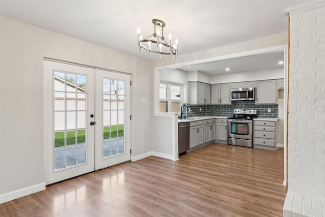 kitchen with appliances with stainless steel finishes, gray cabinetry, decorative backsplash, decorative light fixtures, and french doors