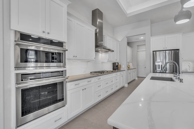 kitchen with appliances with stainless steel finishes, sink, white cabinets, backsplash, and wall chimney range hood