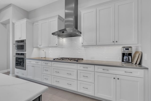 kitchen with stainless steel appliances, white cabinetry, wall chimney range hood, and backsplash