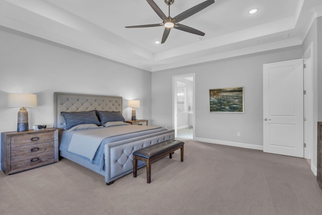 bedroom with ceiling fan, ensuite bathroom, a tray ceiling, and carpet floors