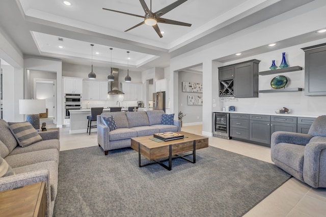 tiled living room with bar, wine cooler, ceiling fan, and a tray ceiling