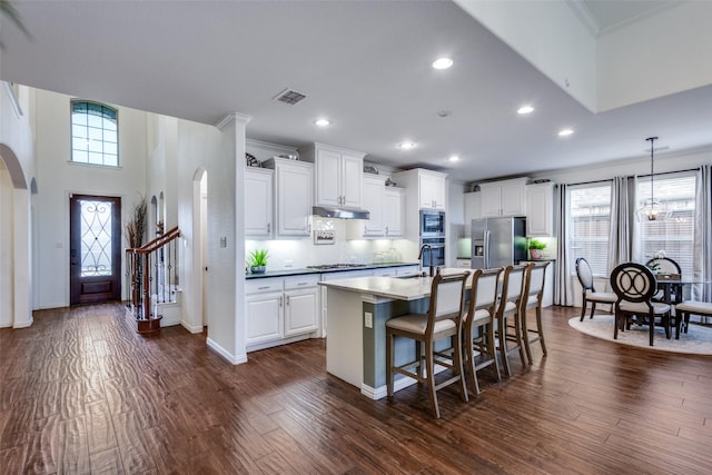 kitchen with white cabinets, a kitchen bar, a kitchen island with sink, stainless steel appliances, and dark wood-type flooring