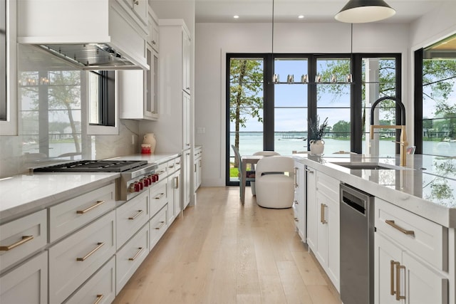 kitchen with premium range hood, white cabinetry, sink, light stone countertops, and a water view