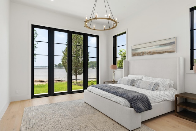 bedroom featuring a water view, a chandelier, and light wood-type flooring