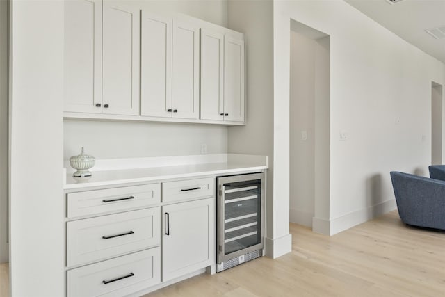 bar with white cabinetry, beverage cooler, and light wood-type flooring