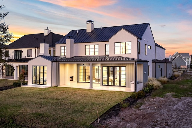 back house at dusk featuring a lawn, french doors, and a patio area