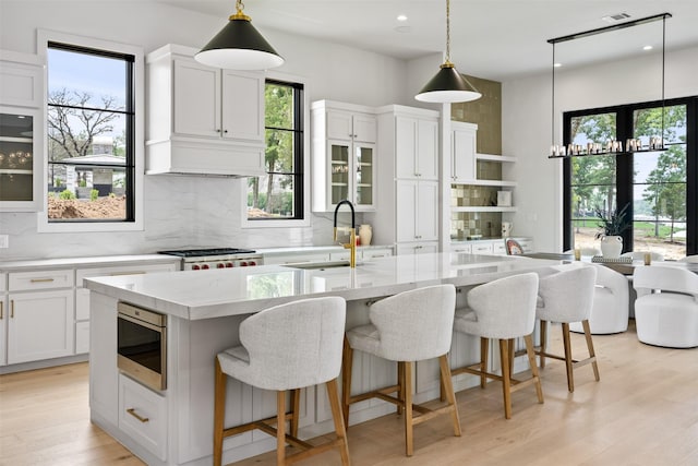 kitchen with light stone counters, a center island with sink, stainless steel microwave, pendant lighting, and white cabinets