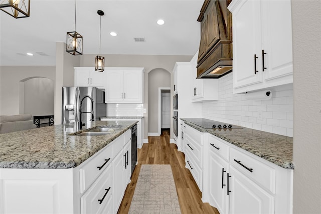 kitchen featuring decorative light fixtures, white cabinetry, sink, a kitchen island with sink, and light stone counters