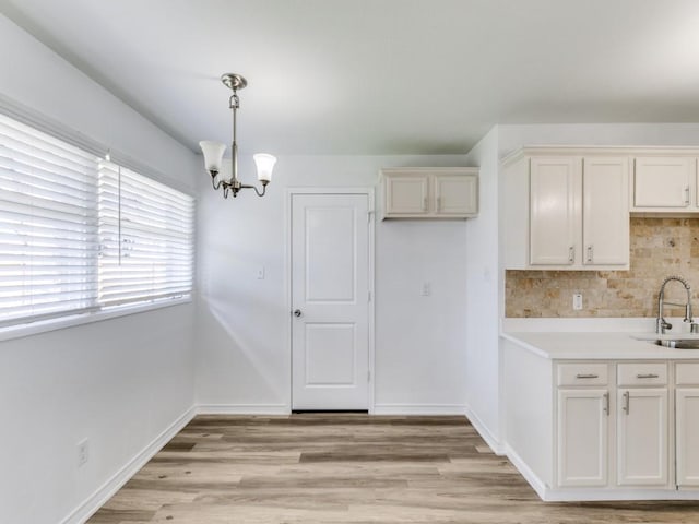 kitchen with tasteful backsplash, white cabinetry, sink, hanging light fixtures, and light wood-type flooring