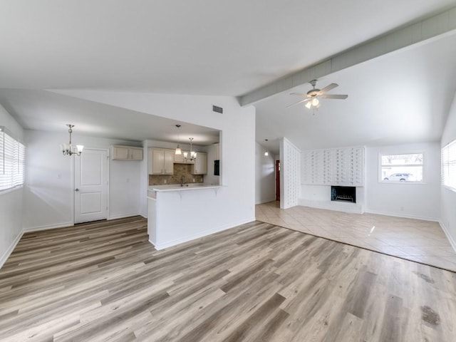 unfurnished living room featuring light hardwood / wood-style flooring, ceiling fan with notable chandelier, vaulted ceiling, and a large fireplace