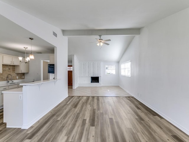 unfurnished living room featuring sink, light hardwood / wood-style flooring, ceiling fan, vaulted ceiling with beams, and a large fireplace
