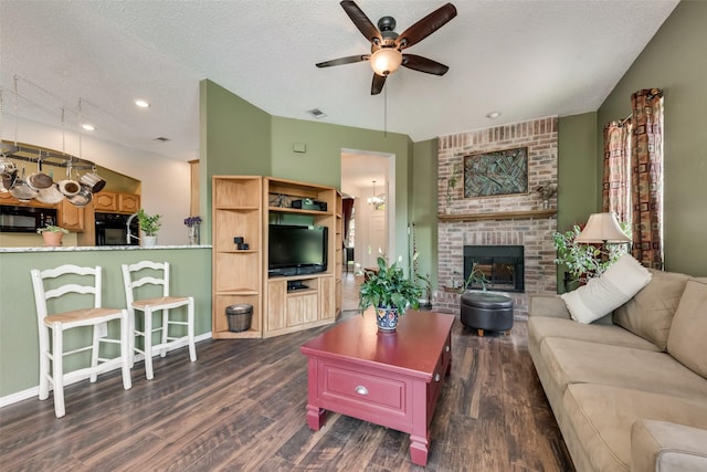 living room with dark hardwood / wood-style floors, ceiling fan, a fireplace, and a textured ceiling