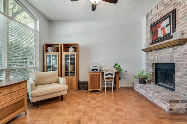 sitting room featuring ceiling fan, a brick fireplace, a textured ceiling, and light parquet floors