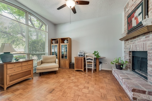 sitting room featuring a brick fireplace, light parquet floors, a textured ceiling, and ceiling fan