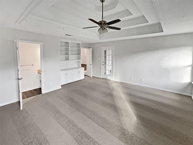 unfurnished living room featuring dark carpet, ceiling fan, and a tray ceiling