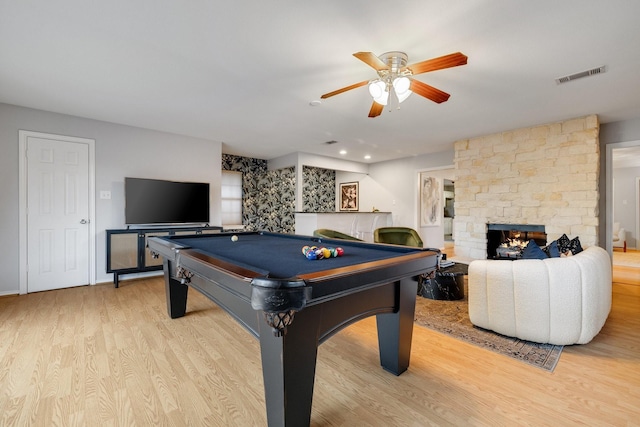 recreation room with a stone fireplace, billiards, ceiling fan, and light wood-type flooring