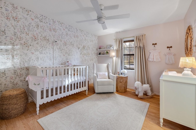 bedroom with ceiling fan, wood-type flooring, and a crib