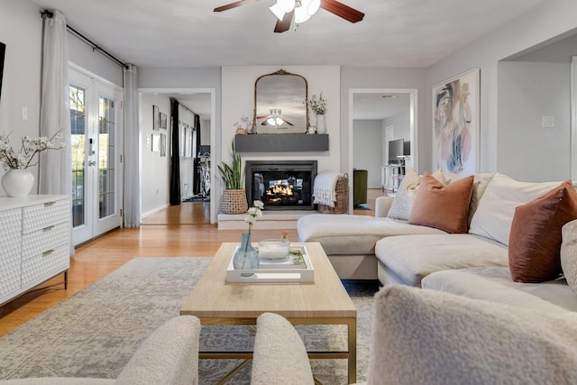 living room featuring french doors, a multi sided fireplace, ceiling fan, and light wood-type flooring