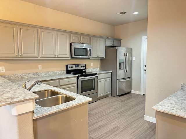 kitchen featuring sink, stainless steel appliances, light stone counters, light hardwood / wood-style floors, and kitchen peninsula