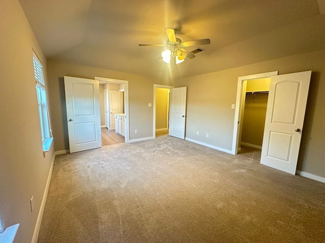 unfurnished bedroom with connected bathroom, a walk in closet, ceiling fan, light carpet, and a closet