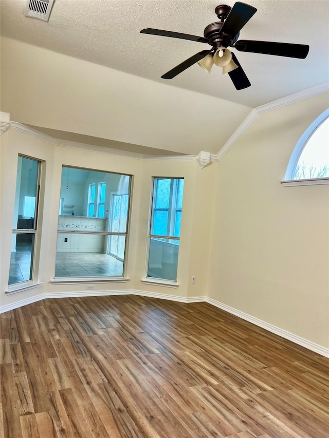 empty room with ornamental molding, lofted ceiling, visible vents, and wood finished floors