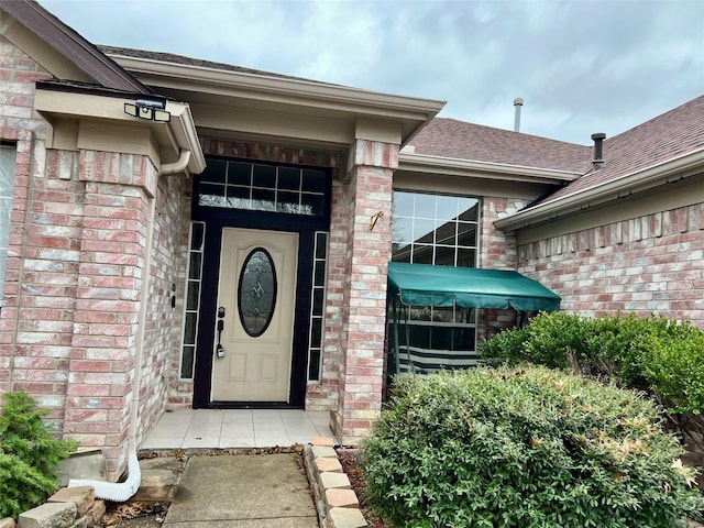 property entrance with roof with shingles and brick siding